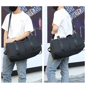Large black travel duffel bag with shoulder strap shown being carried by a model