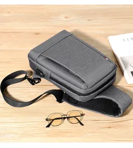 Gray oxford sling bag with built-in USB charging port shown on a wooden desk detail