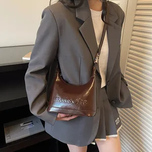 Brown patent leather underarm bag with embossed letters and minimalist curved structure