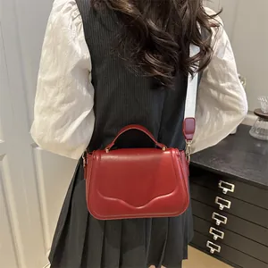 Chic red square crossbody bag with wide fabric strap shown on model in grey dress