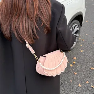 Pink velvet shell bag with pearl handle worn by model over a black blazer
