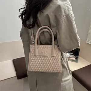 Quilted beige tote bag with gold bow detail and adjustable strap shown on shoulder