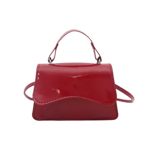 Mini borsa quadrata rossa lucida con manico e tracolla su sfondo bianco pulito