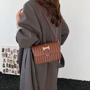 Petit sac carré tressé marron foncé avec boucle H dorée porté à l'épaule par un mannequin