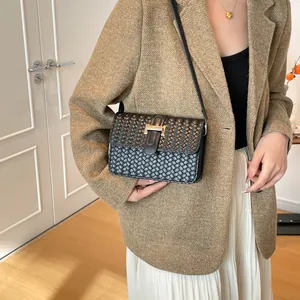 Sac à bandoulière tressé noir avec boucle dorée en H porté par un mannequin à domicile