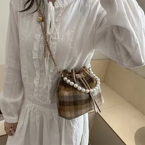 Chic plaid bucket bag with pearl handle and chain strap worn by a model in soft light
