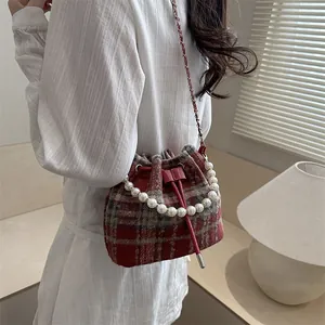 Chic tweed bucket bag with pearl handle and red chain strap shown in a lifestyle setting