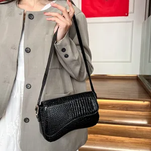 Classic black crocodile pattern handbag with glossy finish worn by a model in a gray suit