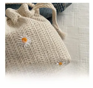 Detailed shot of white daisy embroidery on beige woven straw bag with drawstring cord