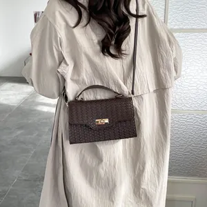 Brown woven crossbody bag with gold twist lock and adjustable strap on a grey trench coat
