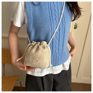 Detail of a beige straw bucket bag with white daisy embroidery and drawstring strap
