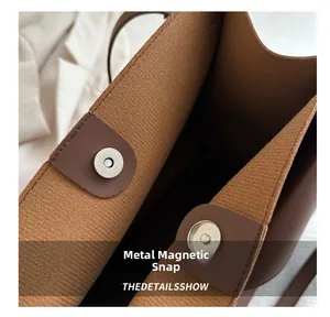 Détail de la boucle magnétique argentée et du cuir marron du sac sous le bras