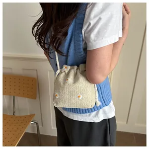 Detail of straw bucket bag featuring embroidered daisies and drawstring closure