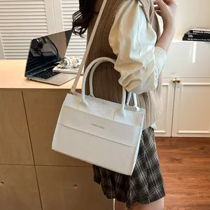White faux leather tote bag with crocodile texture and gold hardware on a desk