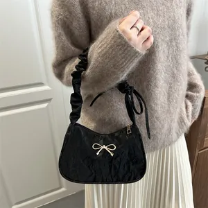 Sac à bandoulière plissé noir avec nœud doré et poignée froncée porté par un mannequin