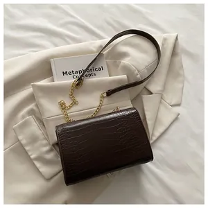 Detail of dark brown faux crocodile texture handbag with gold chain strap on fabric