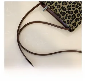 Close-up of leopard print bag with brown leather shoulder strap and silver metal zipper