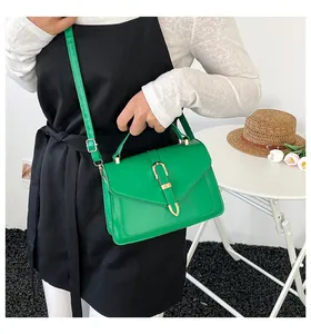 Green leather small square handbag with gold U-shaped buckle shown on model in casual setting