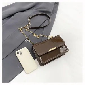 Detail of dark brown patent leather bag with gold chain strap on grey blazer