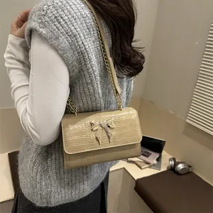 Beige crocodile embossed shoulder bag with butterfly detail shown on a model in urban setting