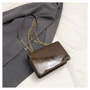Detail of a brown patent leather crossbody bag with a gold metal chain strap on a blazer