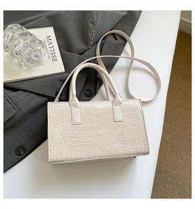 Detail of beige crocodile pattern handbag showing bottom metal studs and dual handles
