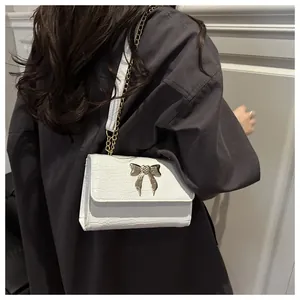 Detail view of white crocodile pattern shoulder bag with a gold butterfly metal clasp