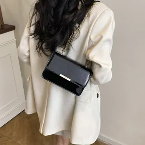 Elegant black patent leather shoulder bag with gold chain strap on ivory blazer