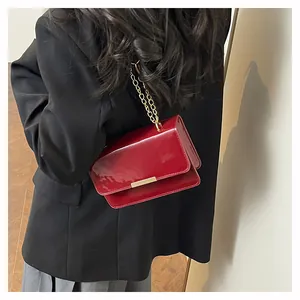 Detail of dark red patent leather crossbody bag with gold chain strap and metal buckle
