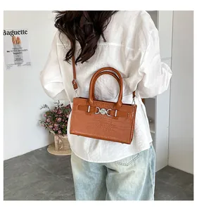 Detail of a brown crocodile pattern handbag with metal ring clasp and adjustable strap