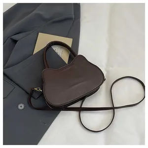 Macro shot of dark brown cat-shaped matte leather handbag with golden metal hardware