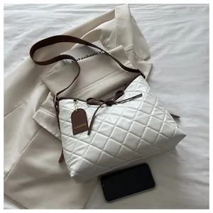 Detail of white quilted tote bag with brown bow accent and leather brand tag