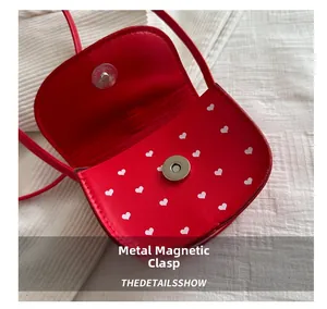 Détail de la fermeture magnétique argentée sur un sac à main rouge à motifs de cœurs