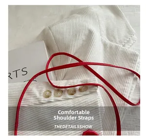 Détail de la bandoulière en cuir rouge sur texture velours côtelé blanc et boutons