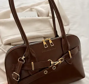 Detail der braunen Tasche mit modischem Schriftzug und goldenen Reißverschlüssen