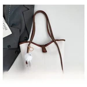 Flat lay of white tote bag with brown straps, plush charm, and fashion magazine props