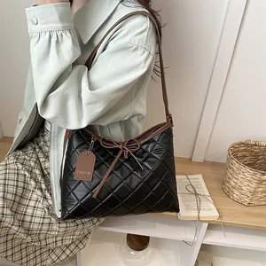Black quilted tote bag with brown bow and shoulder strap in a stylish casual setting