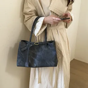Large dark grey retro bucket tote bag in matte suede finish worn with a beige trench coat