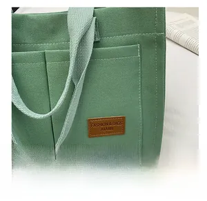 Detail of green canvas tote bag featuring front pockets and brown leather logo tag