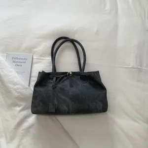 Top view of deep gray suede bucket bag with gold buckles on a white fabric background