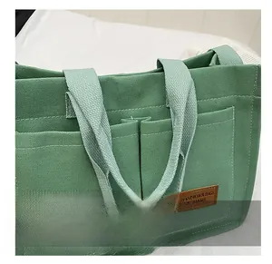 Detailed close-up of light green canvas tote bag with brown leather brand label