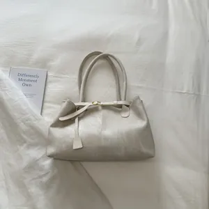 Detailed top view of a creamy white minimalist tote bag with gold hardware on soft fabric