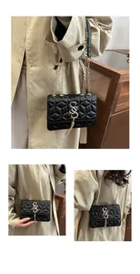 Detailed view of black quilted crossbody bag with gold S-logo and metal chain strap