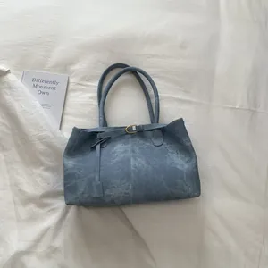 Close-up of vintage blue washed leather tote bag with metal buckle and side tag detail