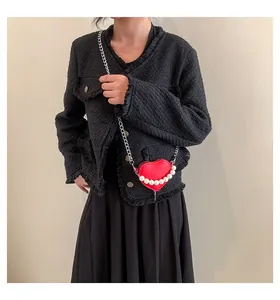 Dettaglio borsa a tracolla rossa a cuore con bordo di perle e catena su giacca in tweed
