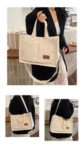 Detail view of large canvas tote bag with front pockets and brown leather brand logo tag