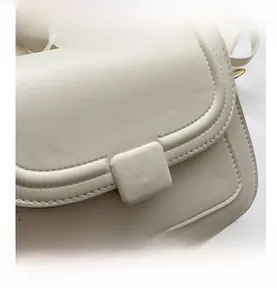 Gros plan sur la texture du cuir crème et les coutures fines d'un sac carré