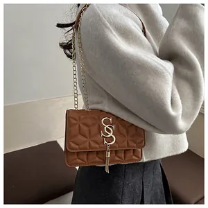 Detail of a brown quilted chain bag with a gold double S buckle and elegant metal tassel