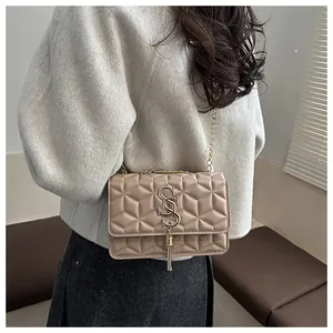 Close-up of quilted beige crossbody bag with gold chain and metal tassel detail