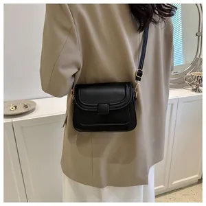 Sac bandoulière noir avec boucle dorée porté par un mannequin pour un style minimaliste